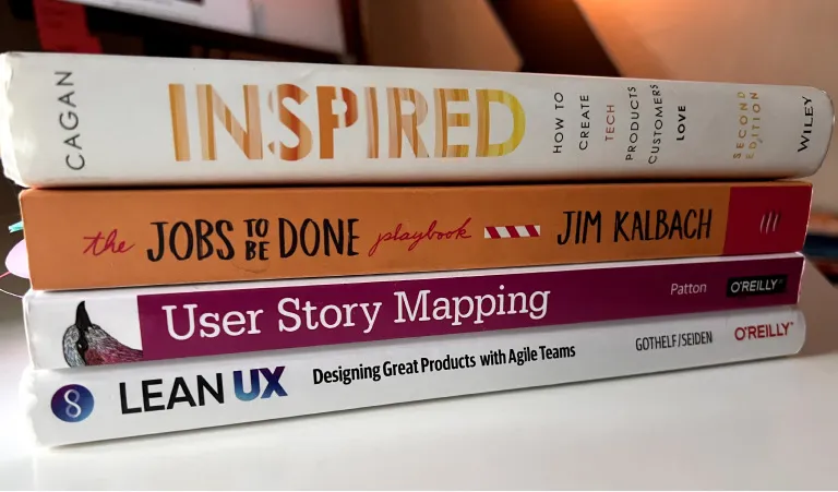 Stack of professional books on product design and user experience, including titles on user story mapping, jobs to be done, and lean UX.